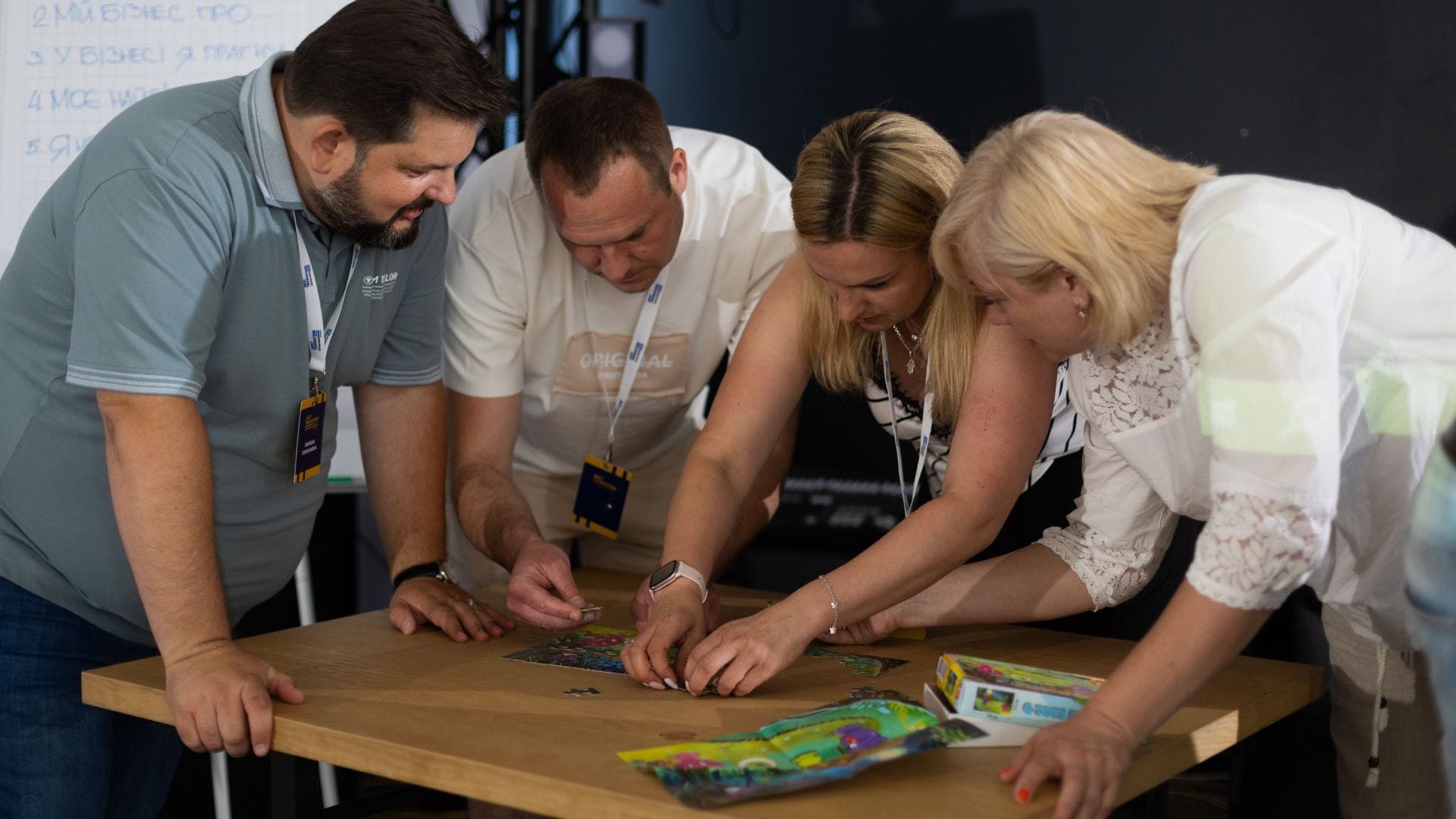 Four people, two women and two men, stand around a table, collaboratively working on a jigsaw puzzle.
